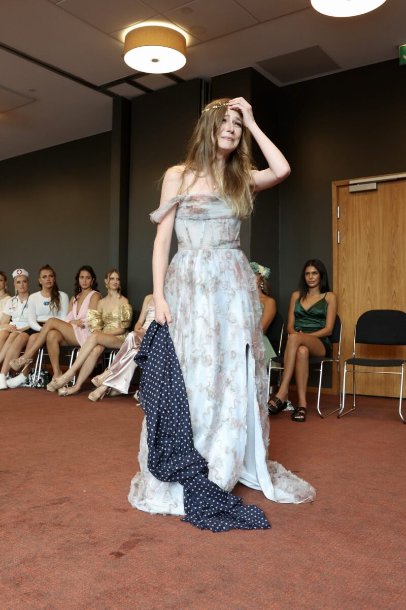 Participant in long floral dress practices her walk while the other participants watch