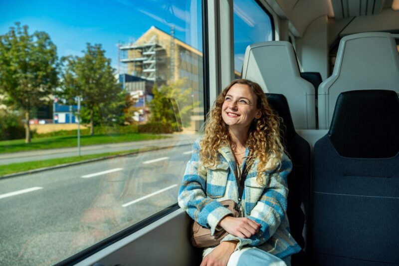 Sille Schnoor sits smiling at the train window in a blue checkered jacket with the landscape rushing past