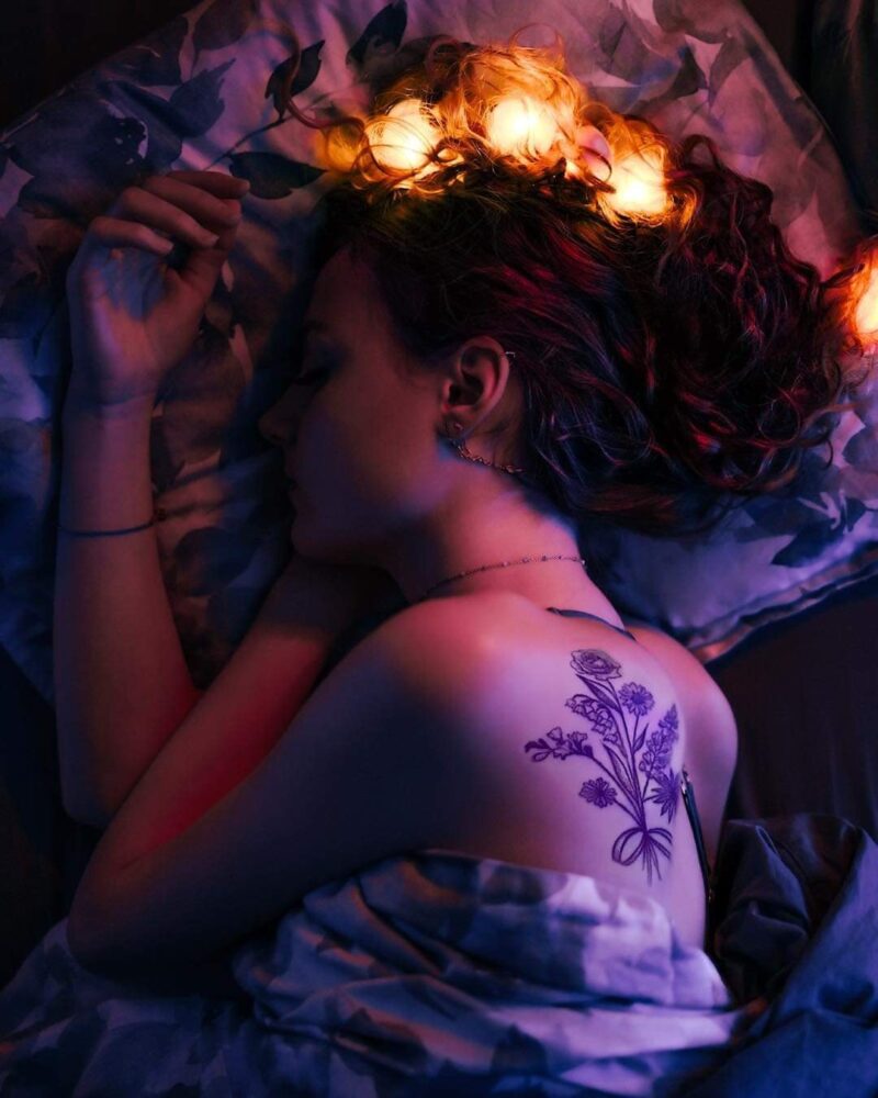 Sille Schnoor lies on her side with candles and flowers in her hair in violet and red light