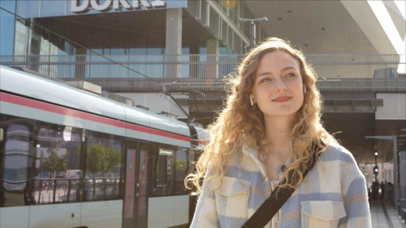 Sille Schnoor stands backlit on a light rail platform with a train in the background