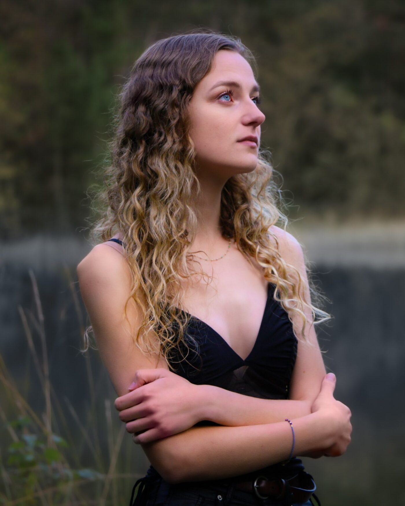 Sille Schnoor with crossed arms in a black top outdoors in front of reeds and water